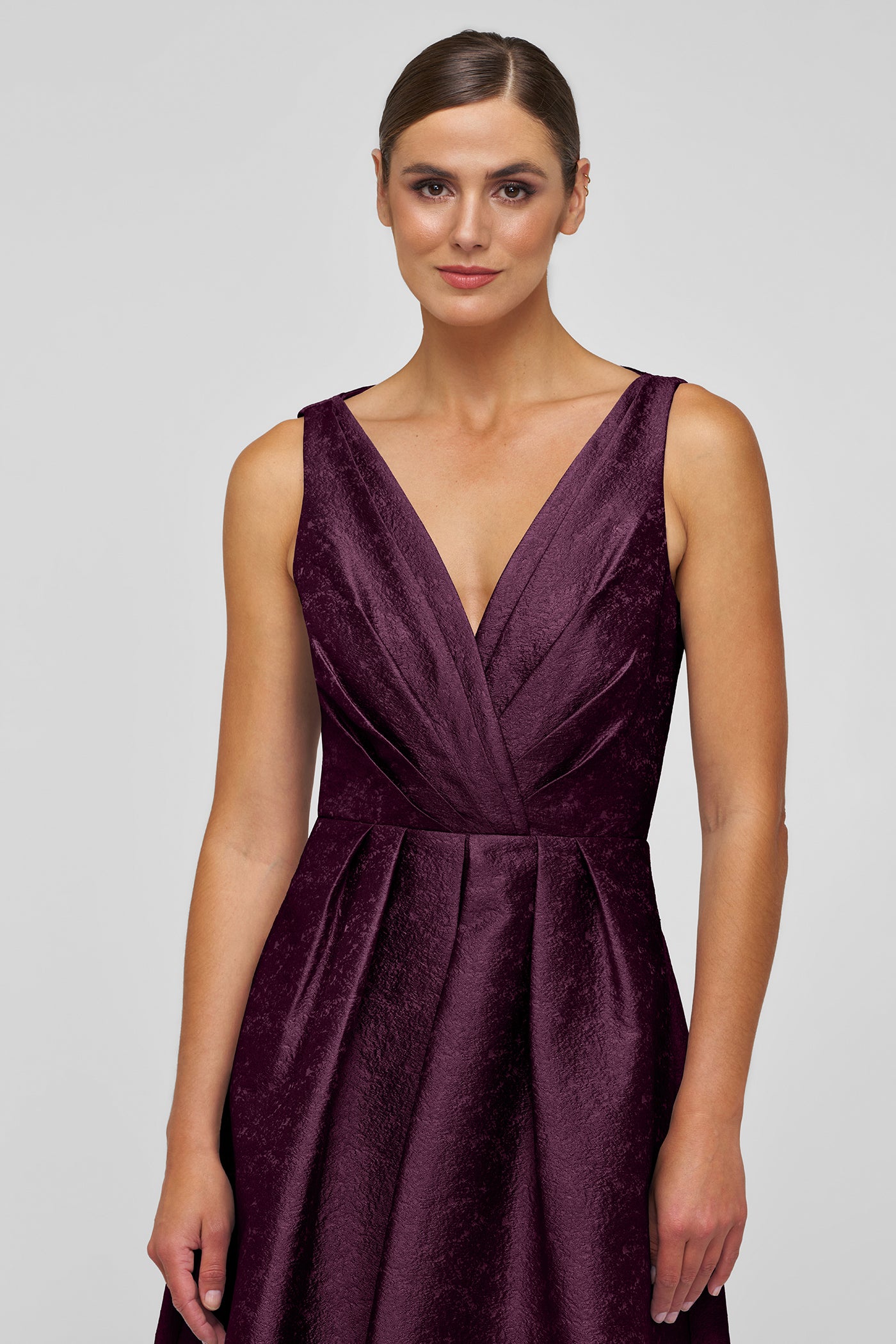Woman wearing a deep purple sleeveless dress on a plain background