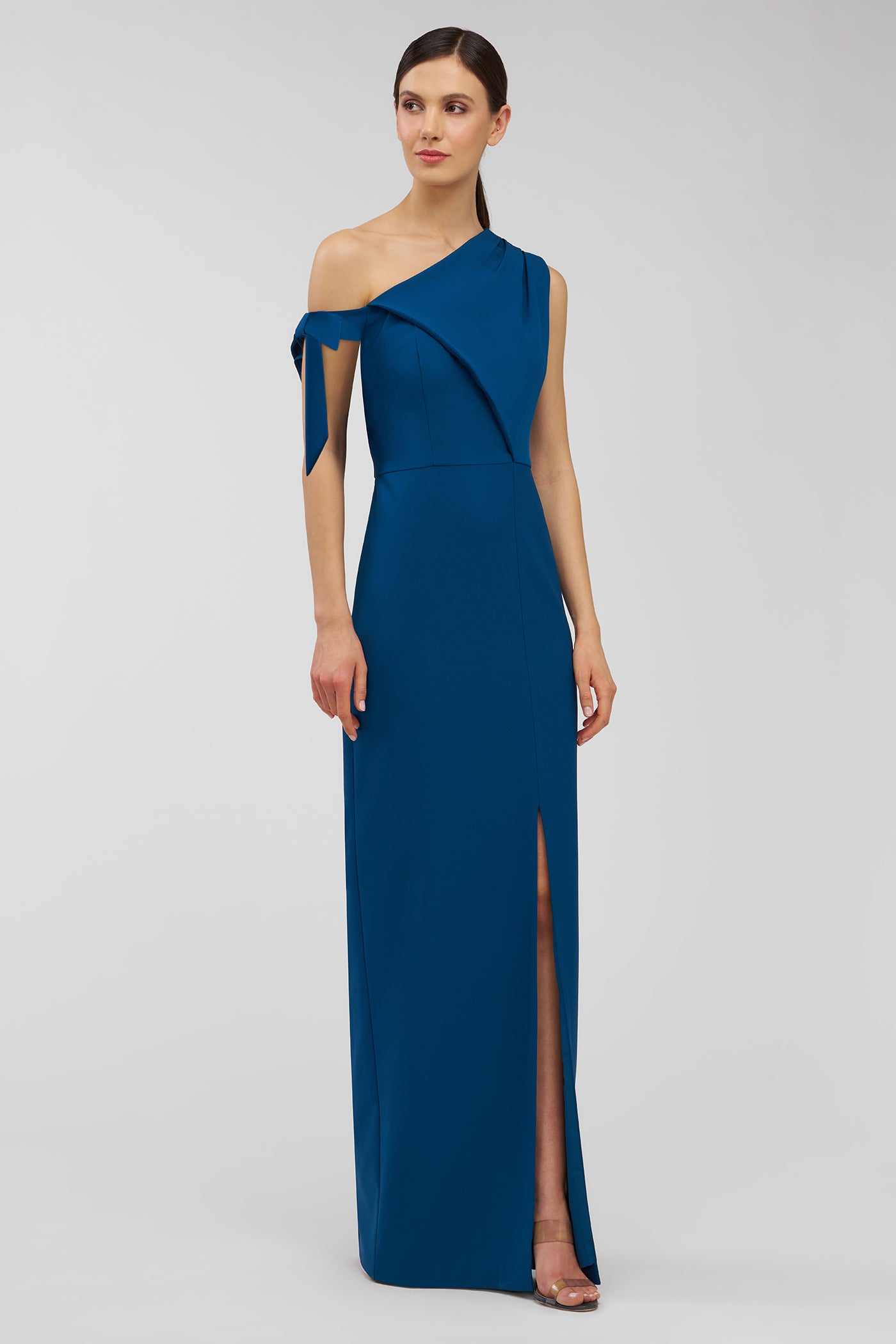 Woman wearing a blue one-shoulder gown with a slit on a gray background