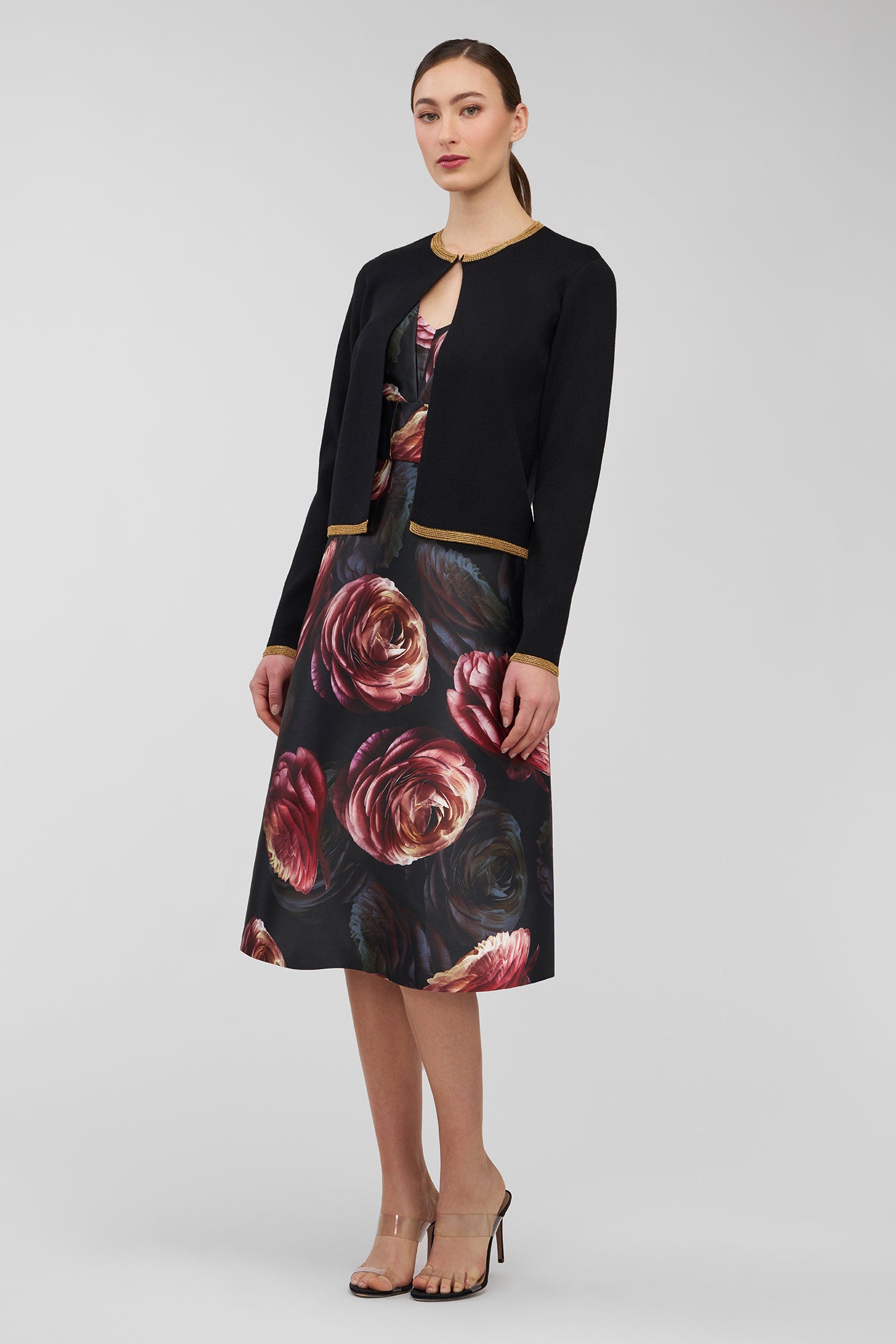 Woman wearing a black floral dress with a black cardigan on a gray background