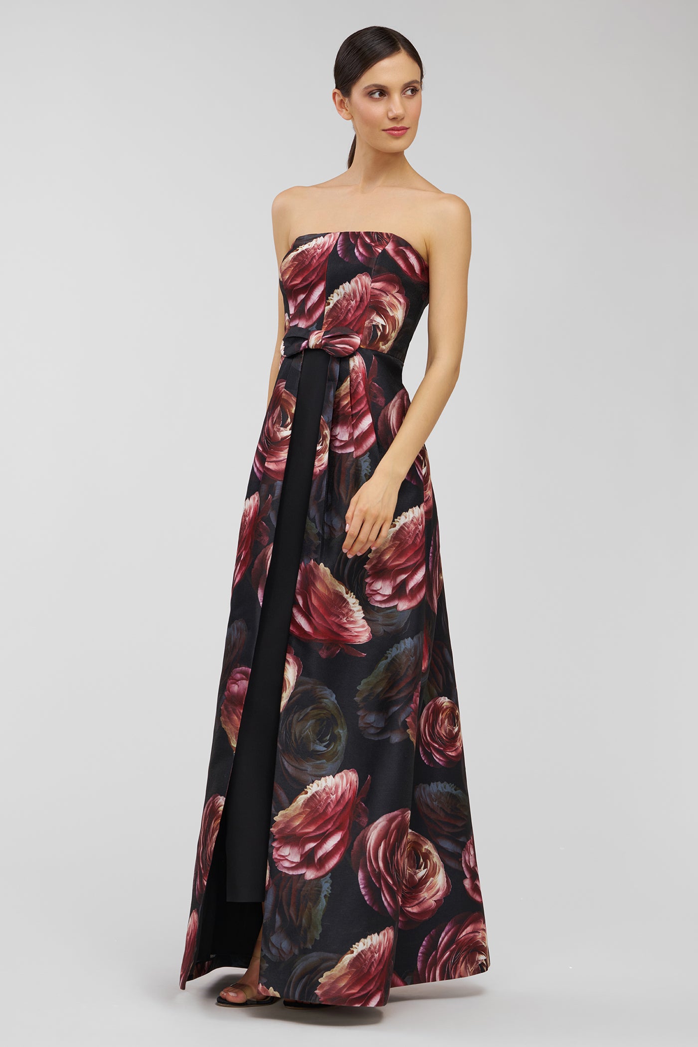 Woman wearing a strapless floral evening gown on a plain background