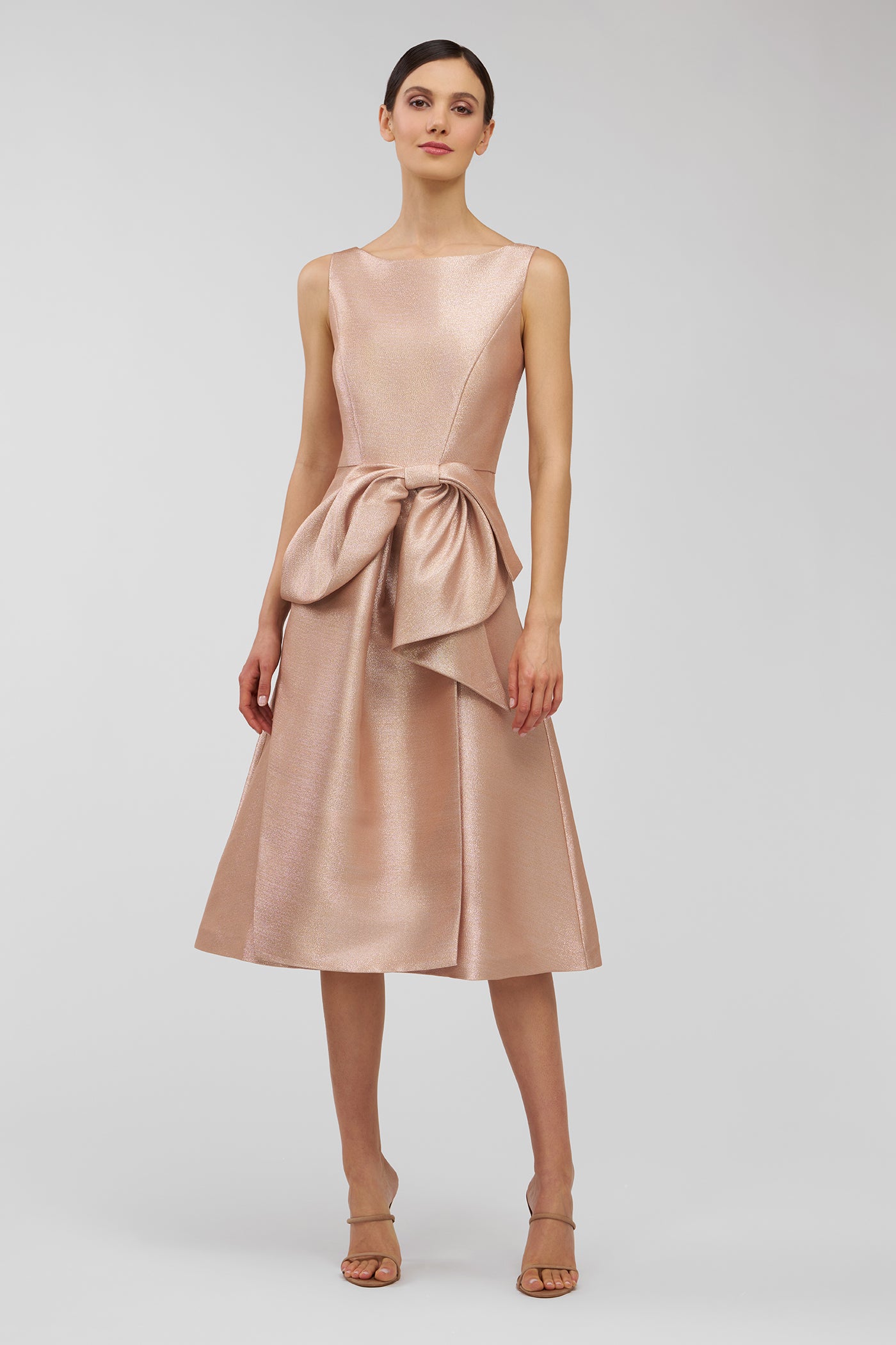 Woman wearing a rose gold dress with a bow detail on a white background