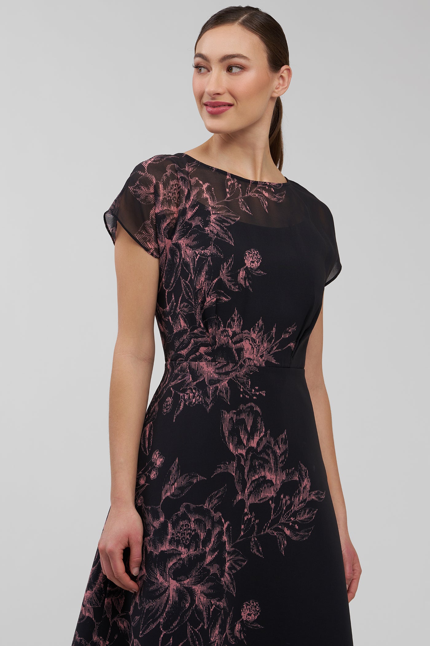 Woman wearing a black dress with pink floral pattern on a plain background