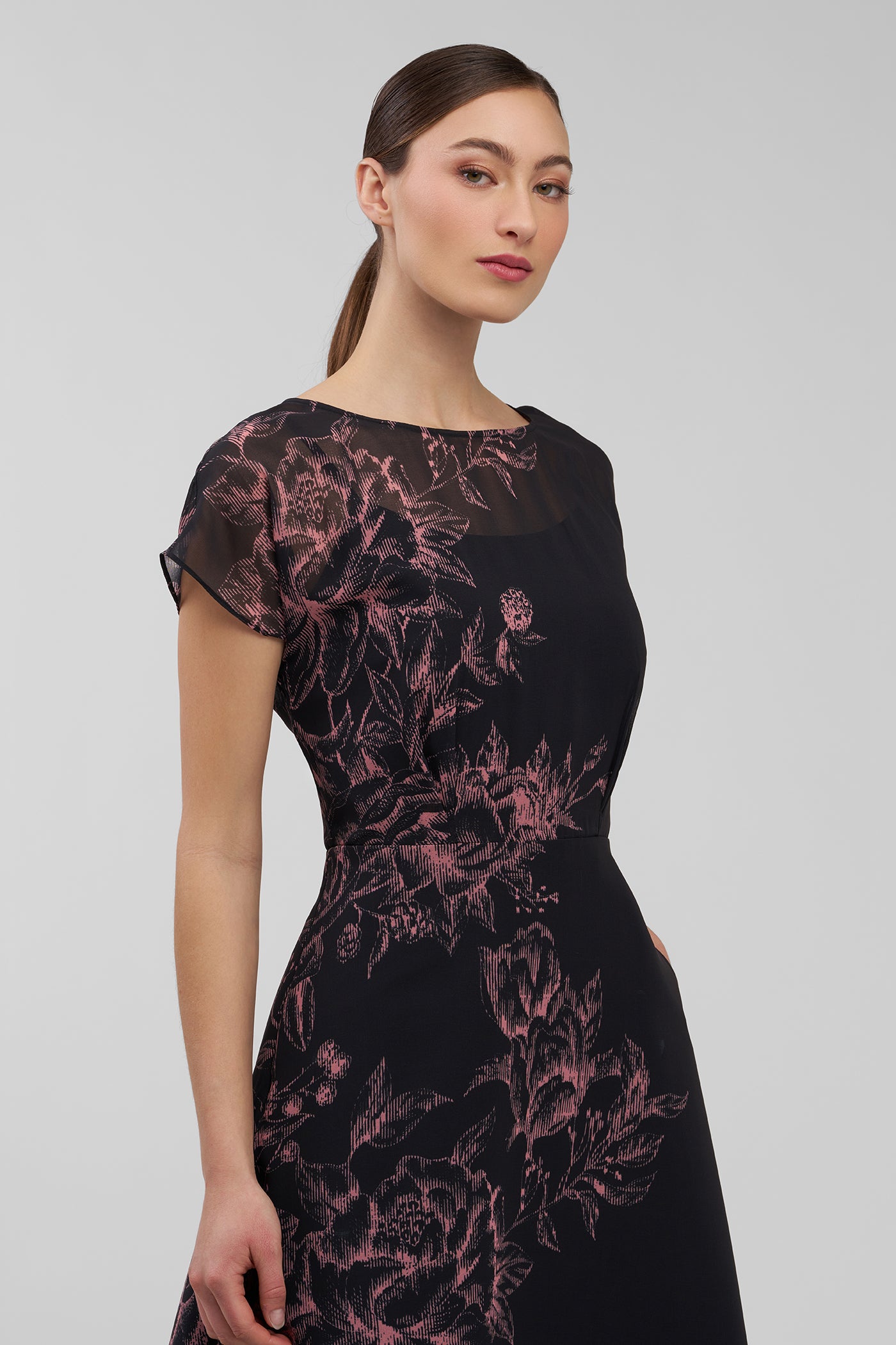 Woman wearing a black dress with pink floral pattern on a gray background