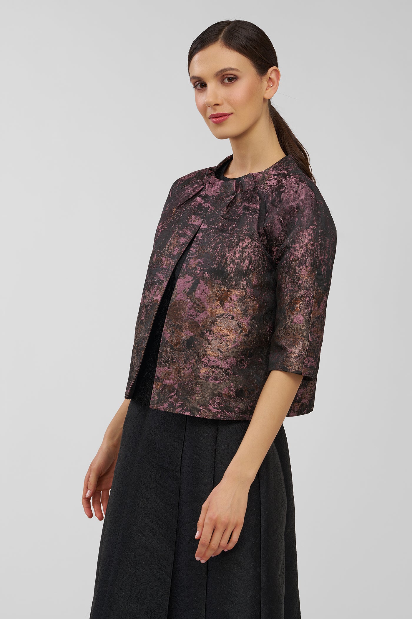Woman wearing a patterned jacket and black skirt on a plain background