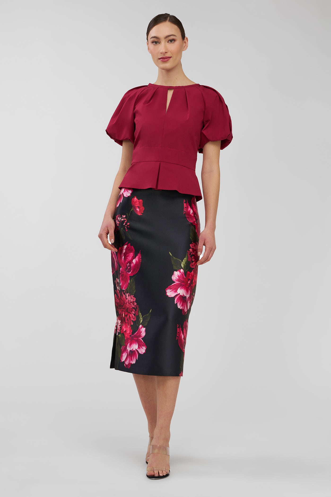 Woman wearing a red blouse and black floral skirt on a white background