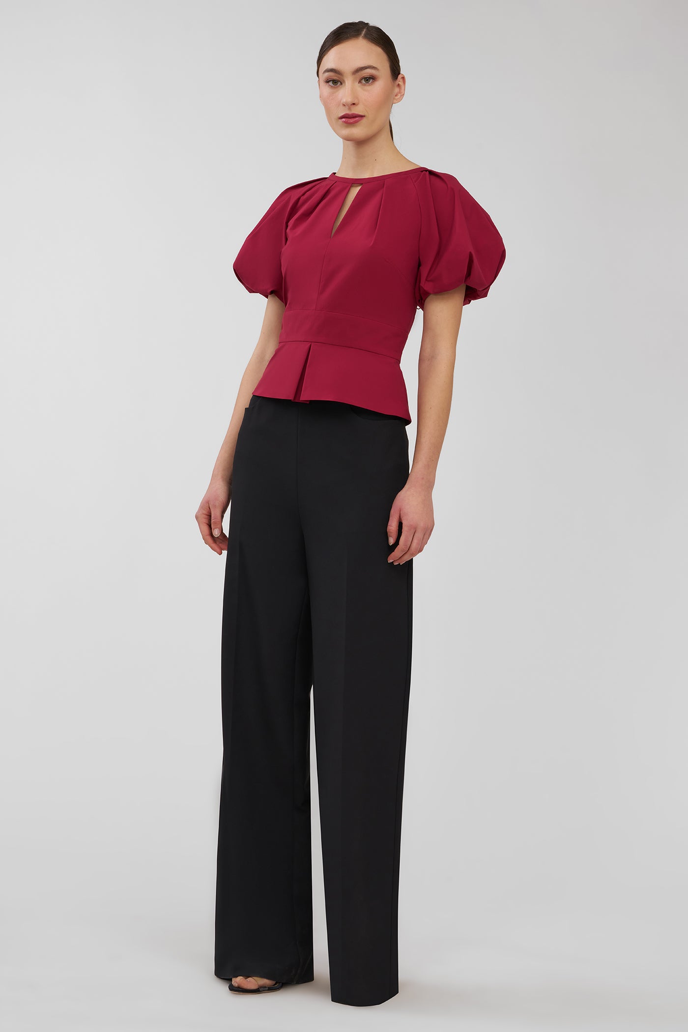Woman wearing a red blouse and black pants on a white background