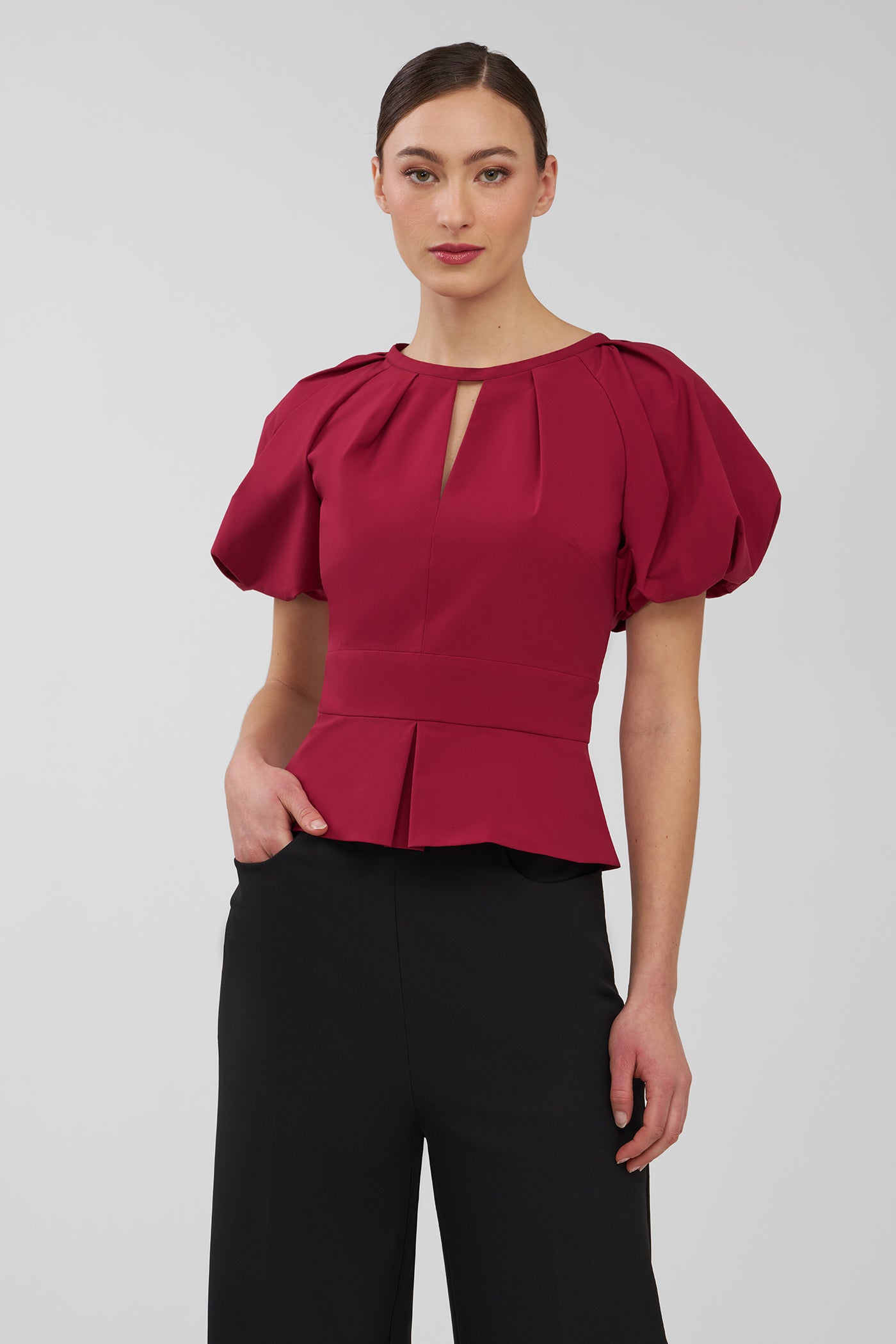 Woman wearing a red blouse with puff sleeves on a plain background