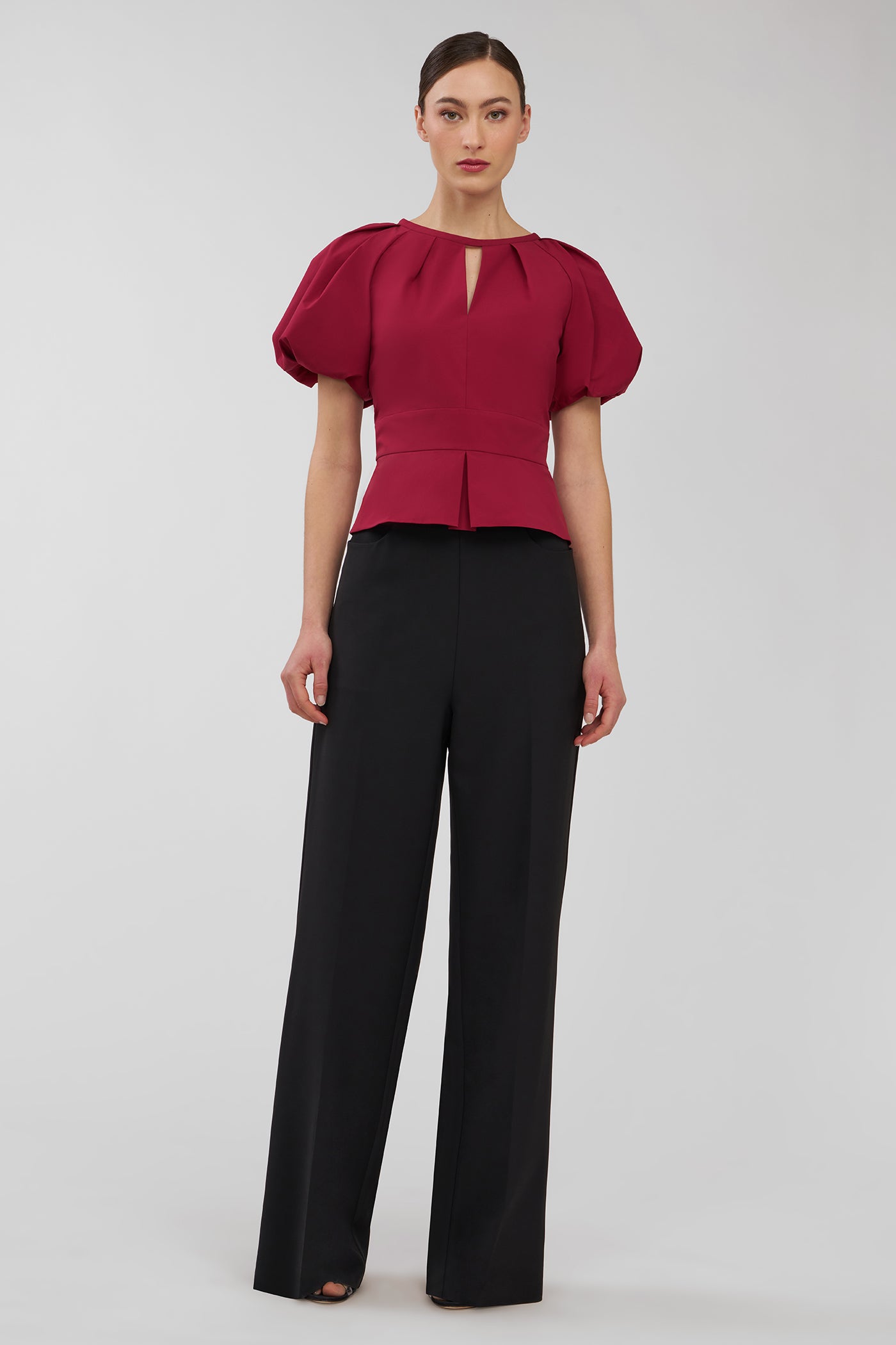 Woman wearing a red blouse with puff sleeves and black pants on a white background