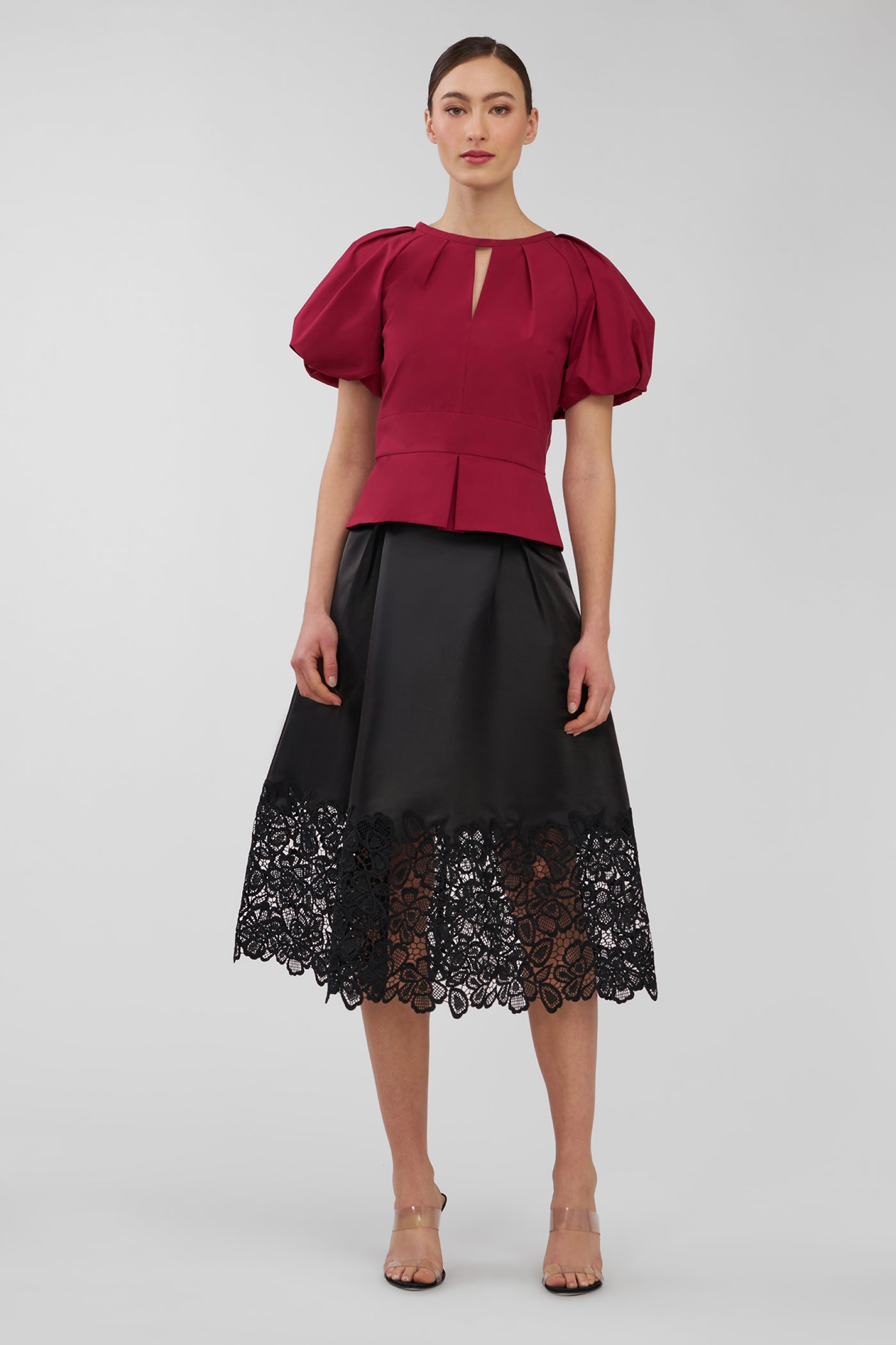 Woman wearing a red top and black skirt with lace hem on a white background