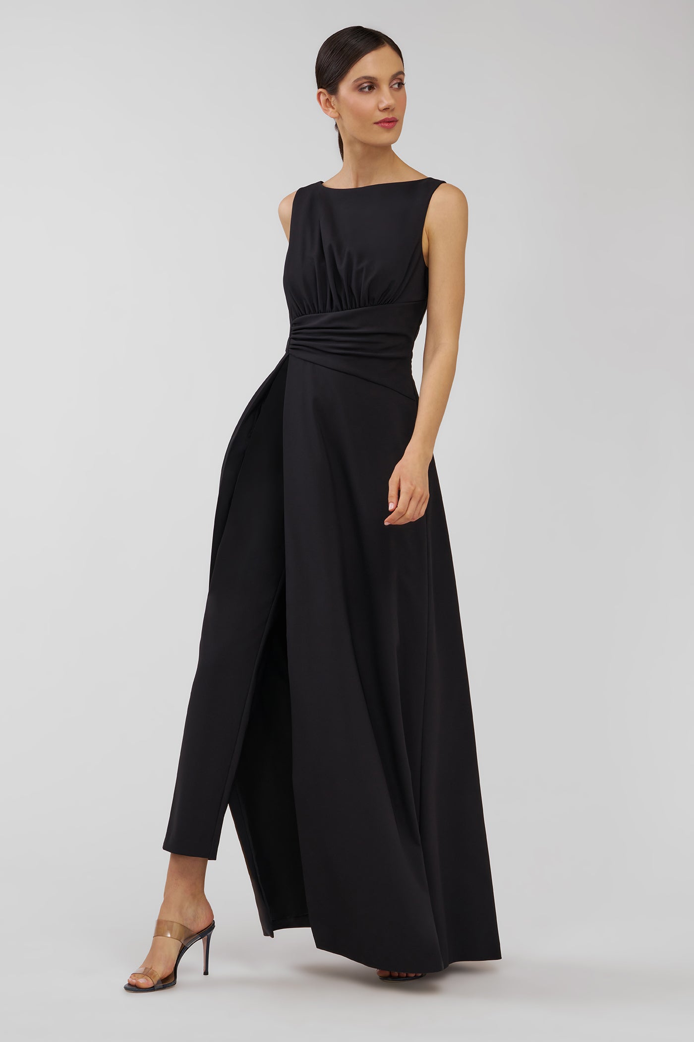 Woman wearing a black sleeveless walk thru jumpsuit on a light gray background