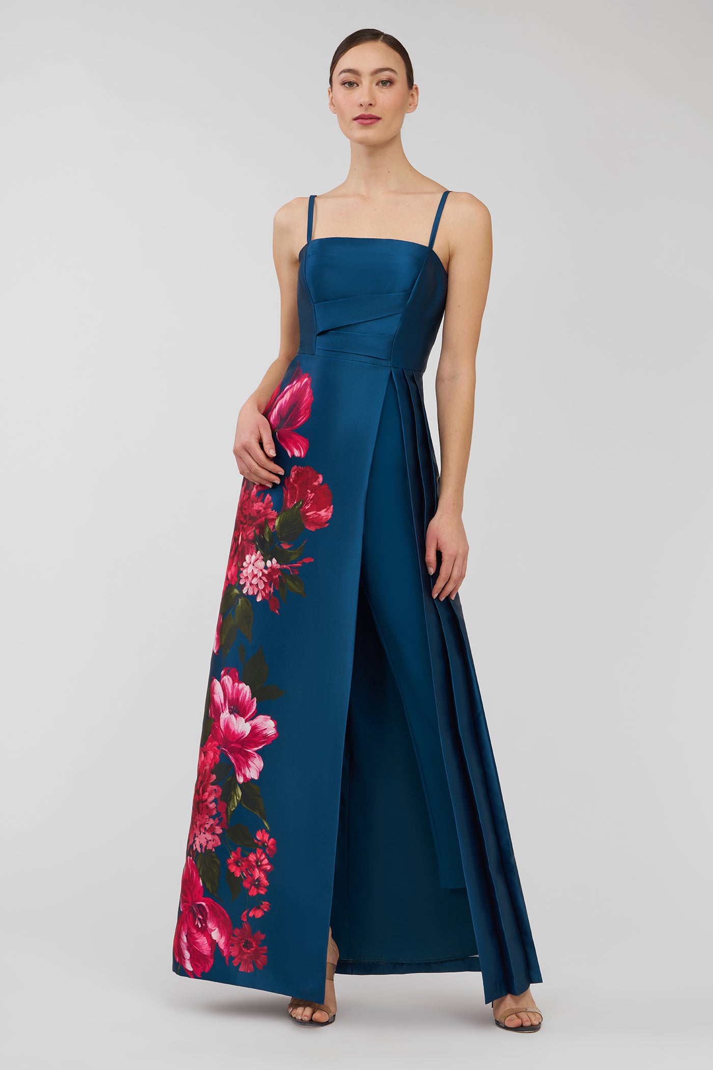 Woman wearing a blue evening walk thru jumpsuit  with floral patterns on a white background