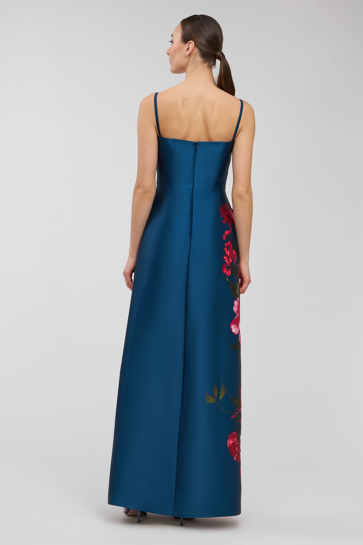 Woman wearing a blue walk thru jumpsuit with floral embroidery on a gray background