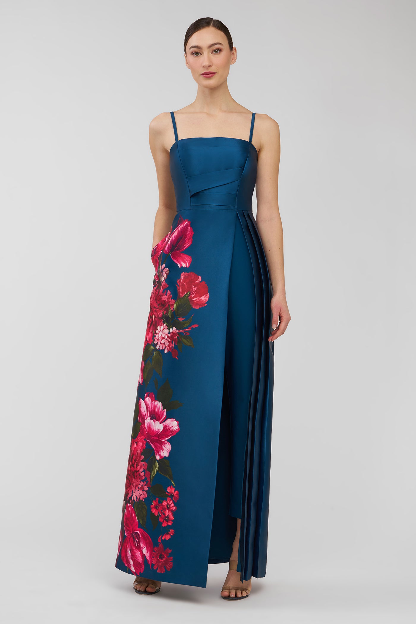 Woman wearing a blue evening walk thru jumpsuit  with floral patterns on a plain background