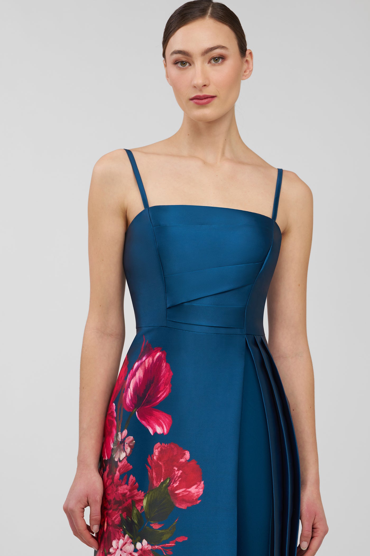 Woman wearing a blue walk thru jumpsuit  with floral patterns on a plain background