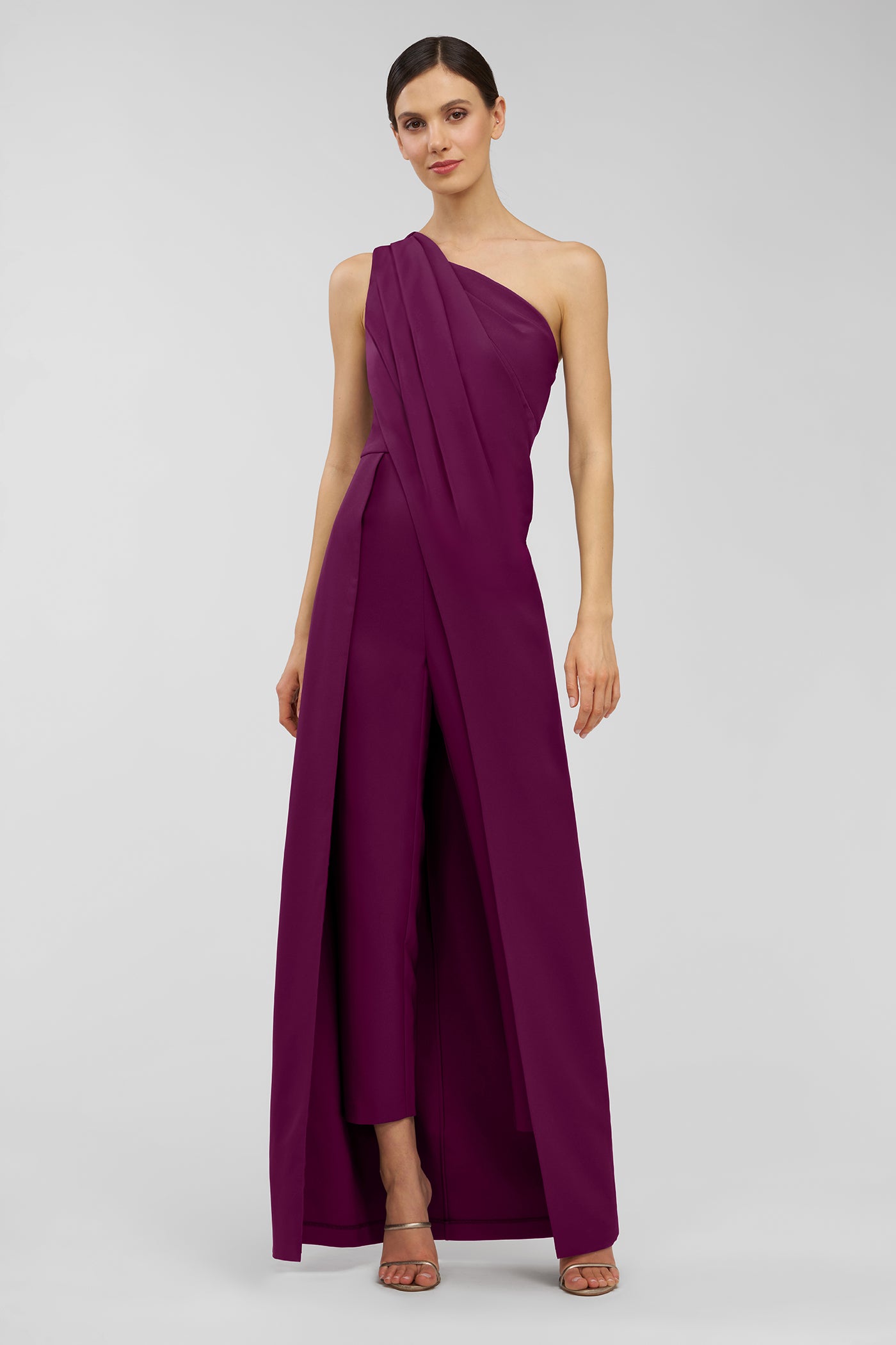 Woman wearing a one-shoulder purple walk thru jumpsuit on a light gray background