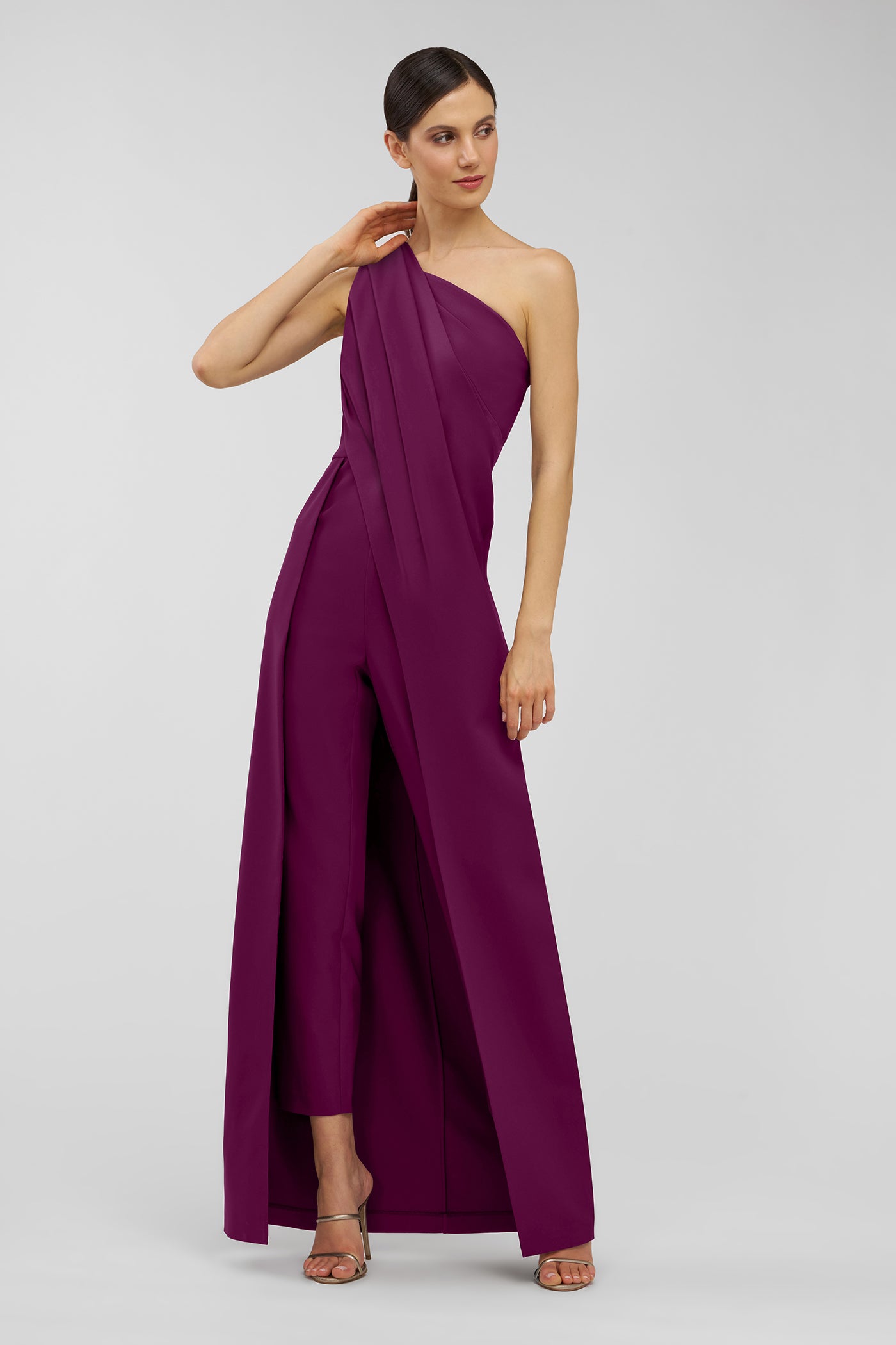 Woman wearing a one-shoulder purple jumpsuit on a light gray background